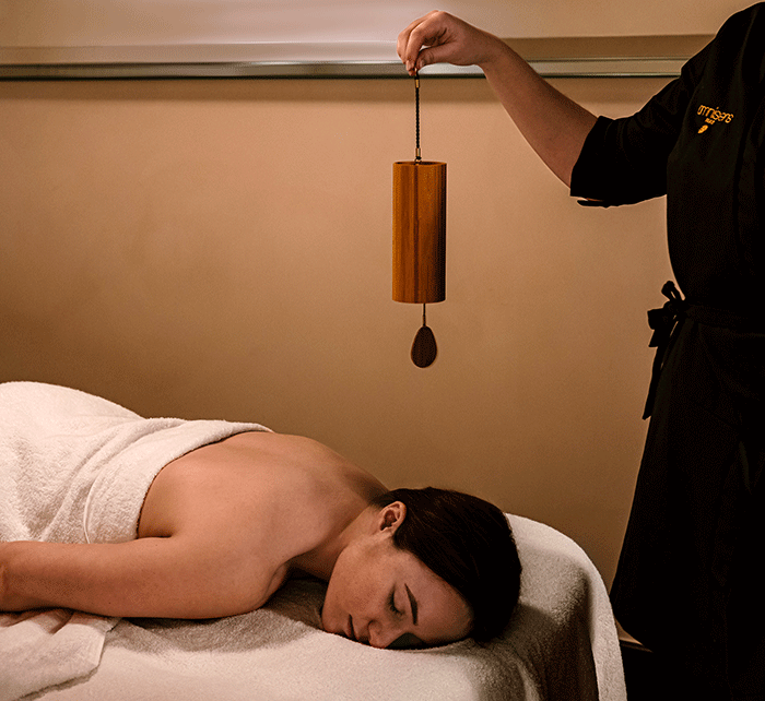 photo d'un soin spa omnisens paris à l'hotel spa chateau des fleurs avec une cliente et une praticienne qui tient un carillon en bois